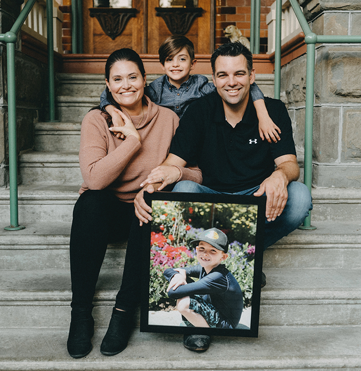 Canuck Place family sitting on the steps of Canuck Place Children's hospice with a framed photo