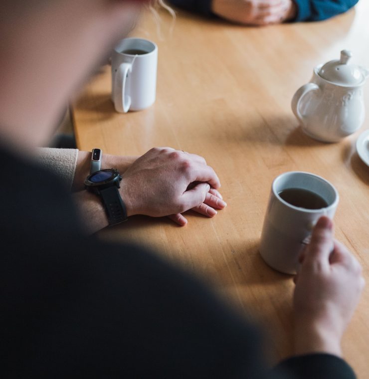 Van Oosterom parents hold hands at the kitchen table, tea and cookies are laid out.