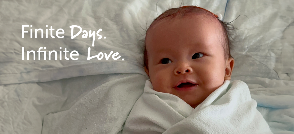 A baby of East-Asian descent with a small tuft of dark hair lies swaddled in a soft white blanket in a hospital crib. The baby has a gentle smile and wide, curious eyes looking to the side. A medical tube is visible in the background. The baby appears calm and comfortable, wrapped snugly in the blanket. The Canuck Place tagline